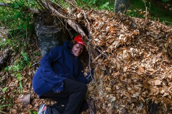 Person liegt in einer Laubhütte aus Ästen und Blättern